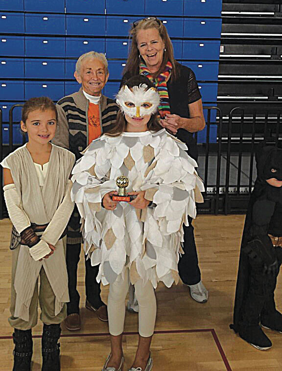 Two children dressed in costumes with adults behind them. One child dressed as a jedi, the other dressed as an owl.